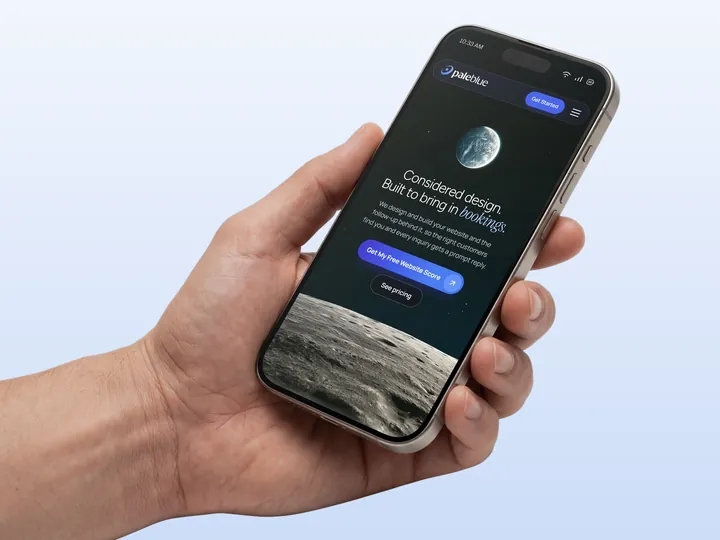 A hand holding a phone showing the Pale Blue homepage